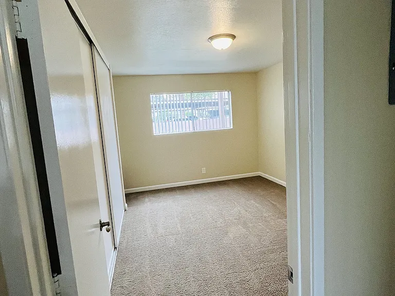 Carpeted bedroom with large window and closet at Plaza Verde Apartments in Escondido, California.