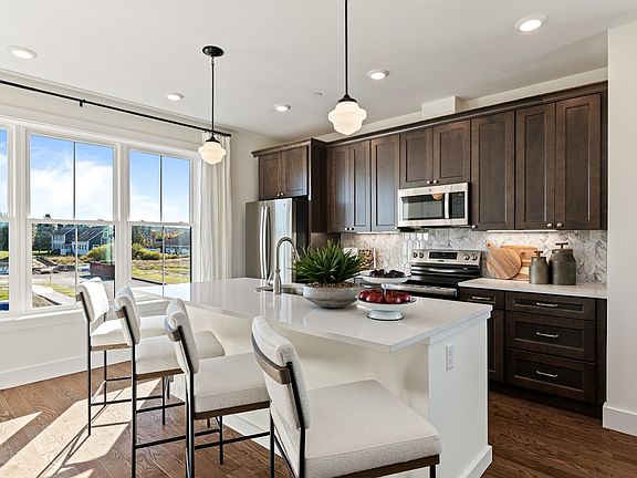 Modern kitchen with dark wood cabinets, white island, pendant lights, and large window with outdoor