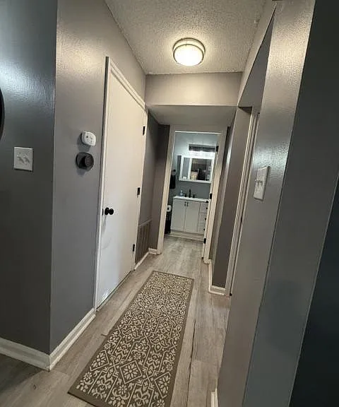 Long hallway with durable plank-style flooring, ceiling light, and easy access to nearby bath vanity and storage doors.