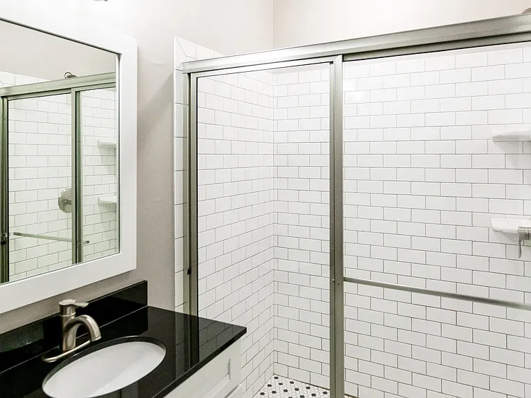 Porcelain tile bathroom with stop-in shower and undermount sink with black countertop