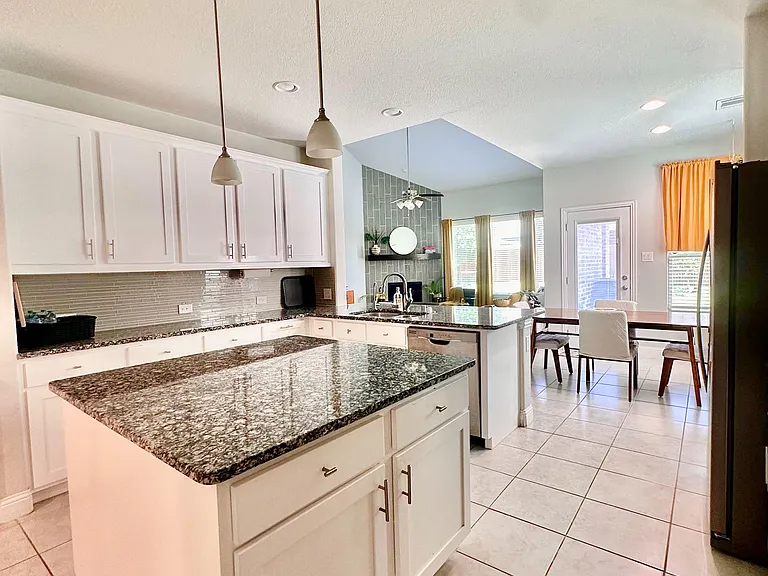 Spacious kitchen with a large granite island, ample white cabinetry, and a connected dining area near a patio door.