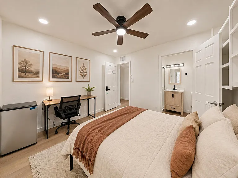 Private bedroom with ceiling fan, work desk, mini fridge, and convenient access to an en-suite vanity and bath area.