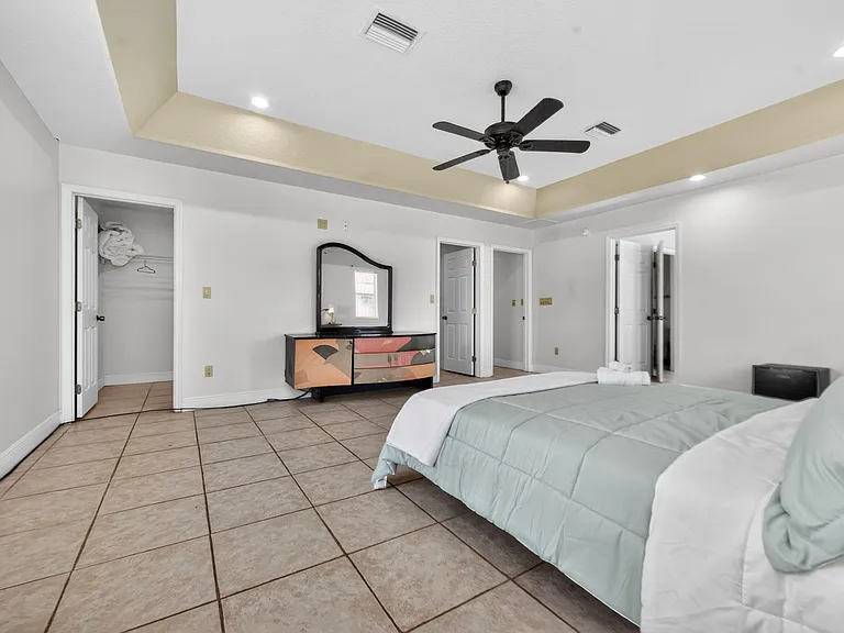 Spacious bedroom with tile flooring, tray ceiling with fan, and a closet plus dresser storage for easy organization.