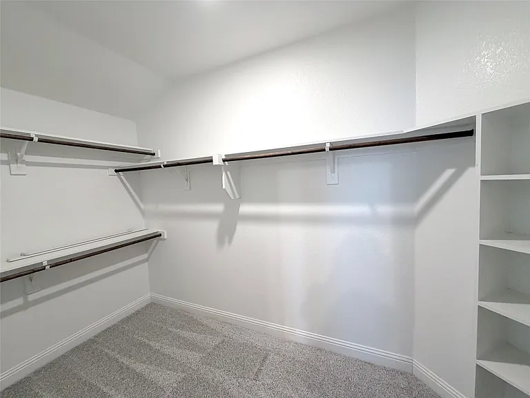 This spacious primary bedroom walk-in closet is designed for optimal organization, featuring extensive dual-level clothing rods that provide ample hanging space, integrated custom built-in shelving units for folded items or accessories, bright recessed ov