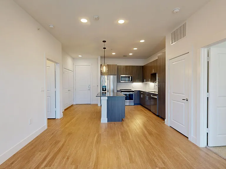 Apartment kitchen with stainless steel appliances, dining and living room with wood-style flooring.
