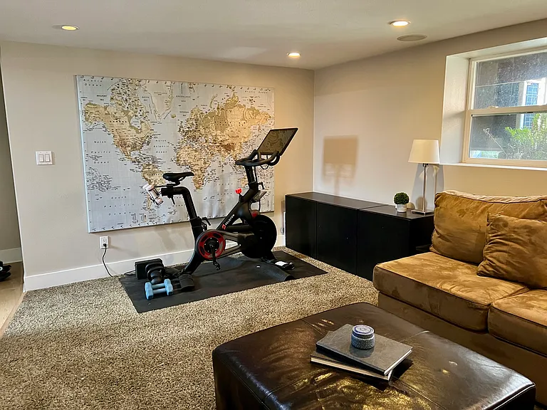 Lower level living room space with built in for tv, room for exercise equipment and L shaped couch.