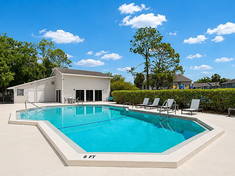 Inviting outdoor pool with sleek lounge chairs surrounded by lush greenery and clear blue skies.