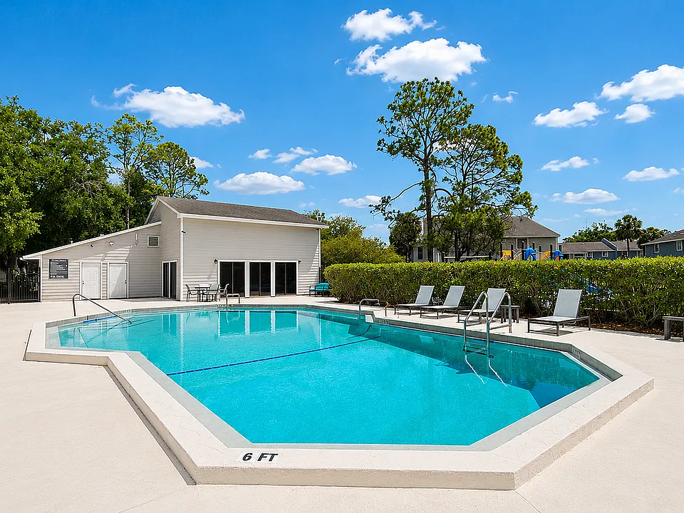 Inviting outdoor pool with sleek lounge chairs surrounded by lush greenery and clear blue skies.