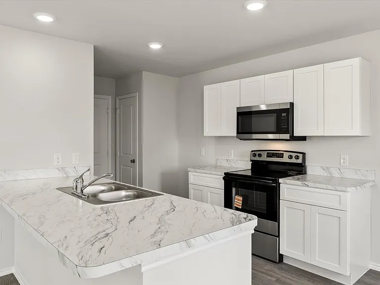 Open-concept kitchen featuring an eat-at island with a double basin sink, white cabinetry, integrated stainless steel appliances, and light-toned countertops