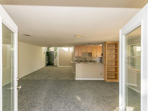 Looking in from double doors to carpeted living room tiled dining area and open kitchen with breakfast bar. Front door in the distance.