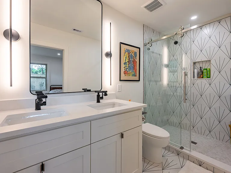 Primary bath featuring dual vanity, designer lighting, and walk-in glass shower with modern tile finishes.