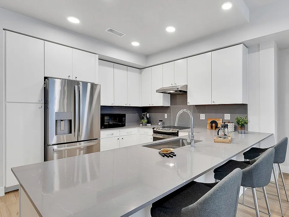 Modern kitchen with sleek white cabinets, stainless steel appliances, elegant countertops, and cozy bar seating.