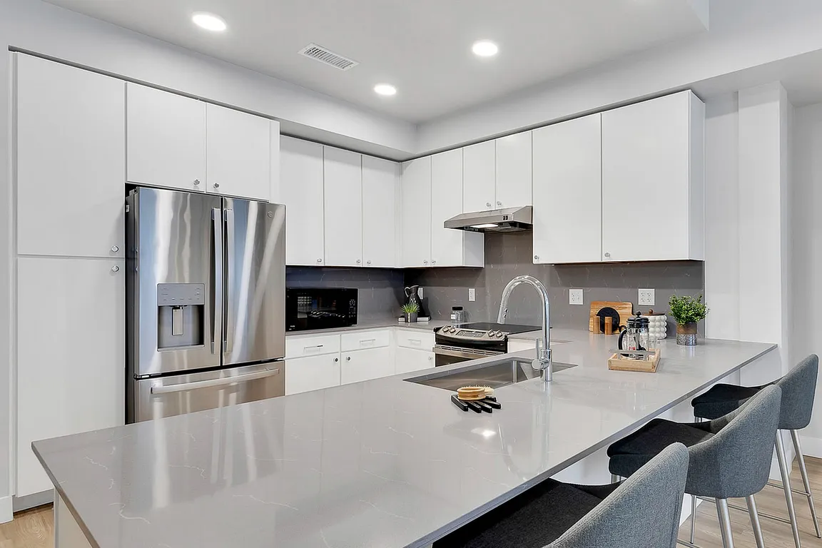 Modern kitchen with sleek white cabinets, stainless steel appliances, elegant countertops, and cozy bar seating.