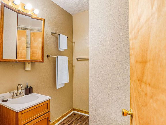A small bathroom featuring a toilet, sink, mirror, and shelves against light-colored walls.