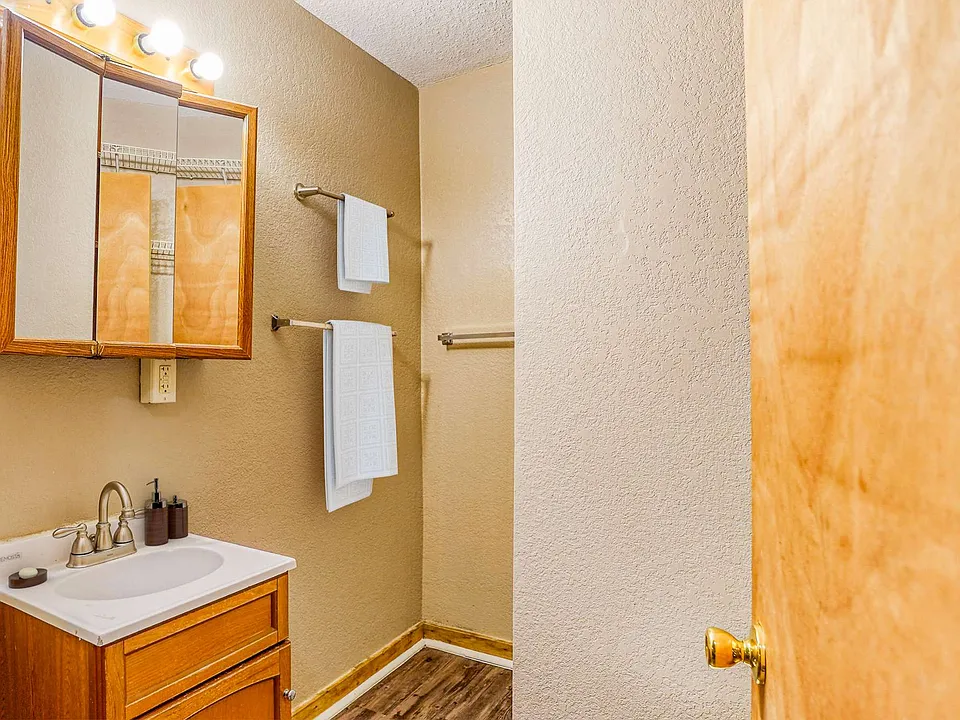 A small bathroom featuring a toilet, sink, mirror, and shelves against light-colored walls.