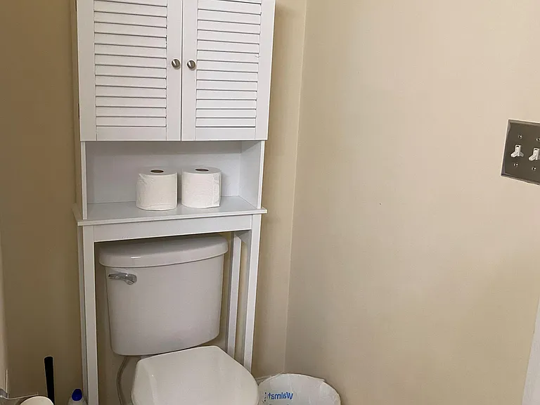 Bathroom area with toilet and over-the-toilet storage cabinet, plus shelving for towels and essentials.