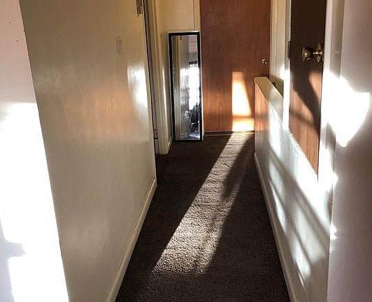 hallway looking from living/kitchen to the bathroom door, bedroom on the left, stairway on the right