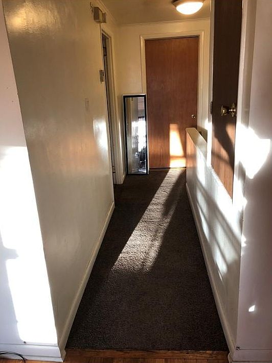 hallway looking from living/kitchen to the bathroom door, bedroom on the left, stairway on the right