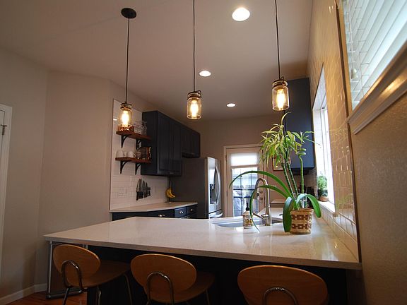 Fully tiled backsplash, quartz countertops, deep sink with rack, and accent shelving.