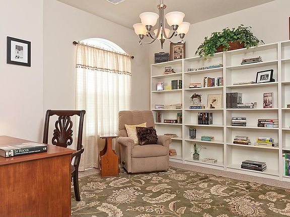 This dining room has a beautiful chandelier, blinds that stay, decorative archway to kitchen, carpet and high ceiling.
