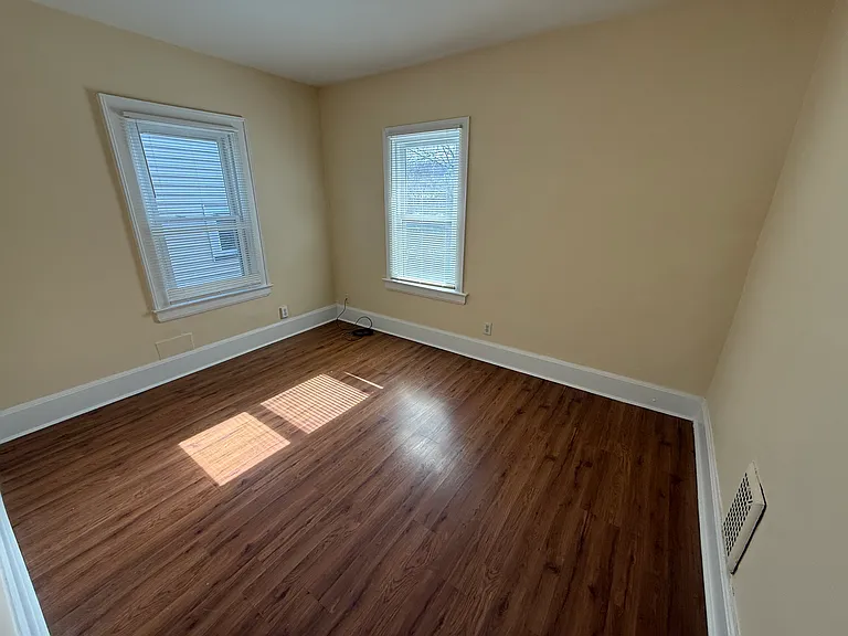 Upstairs rear bedroom. Windows face left (over the landscaped pathway) and another facing the rear of the building. Walls and moulding freshly painted in 2025. There is no closet in this bedroom.