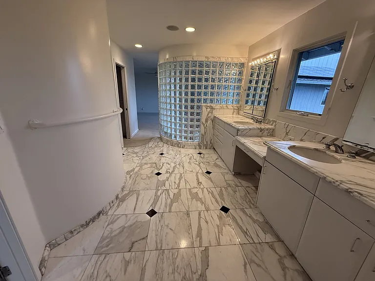 In-suite primary bathroom is tastefully appointed with glass block walls featuring dual sinks, Jacuzzi tub, multi-jet shower stall, a bidet, and a walk-in closet with built-in organized storage.