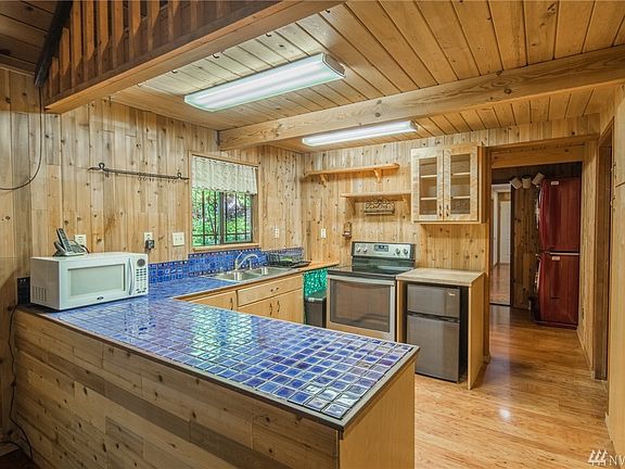 Cabin kitchen with tile counters & double sink! Included appliances- microwave, dishwasher, stove/range, mini fridge + full size fridge, washer/dryer, & extra freezer in garage loft too!