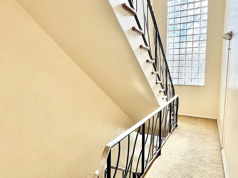 Elegant staircase with artistic railing and large window, offering abundant natural light in a modern home.