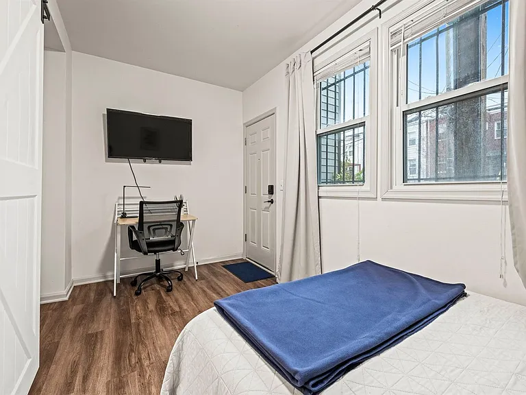 Bedroom with large windows, wood-style flooring, and a dedicated desk area plus wall-mounted TV for work and downtime.