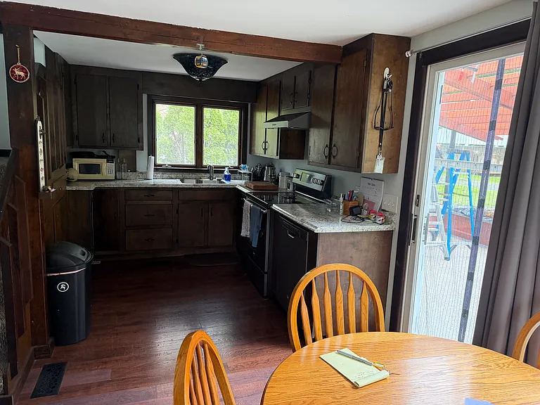 Kitchen side with fridge, space of dinner table with sliding glass door to outdoor concrete patio space.