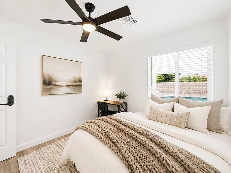 Well-appointed bedroom with a ceiling fan, generous window with blinds, and a dedicated desk nook for work or study.
