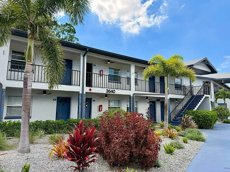 Inviting two-story apartment with lush landscaping and palm trees under a clear blue sky.