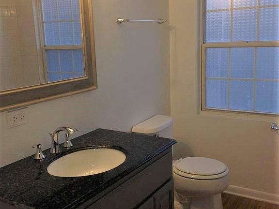 Large bathroom with wood grain floors, stylish gray vanity with granite top, natural light and a tub/shower combo.