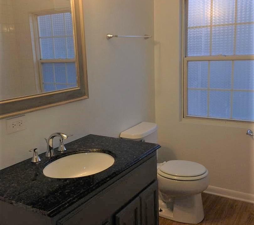Large bathroom with wood grain floors, stylish gray vanity with granite top, natural light and a tub/shower combo.