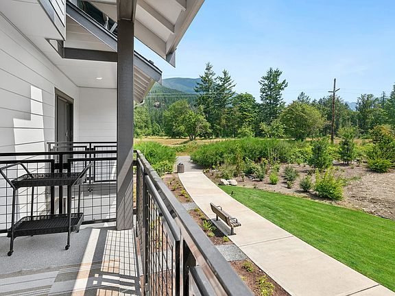 A modern, multi-story building with a balcony overlooking a well-manicured lawn and a lush, forested