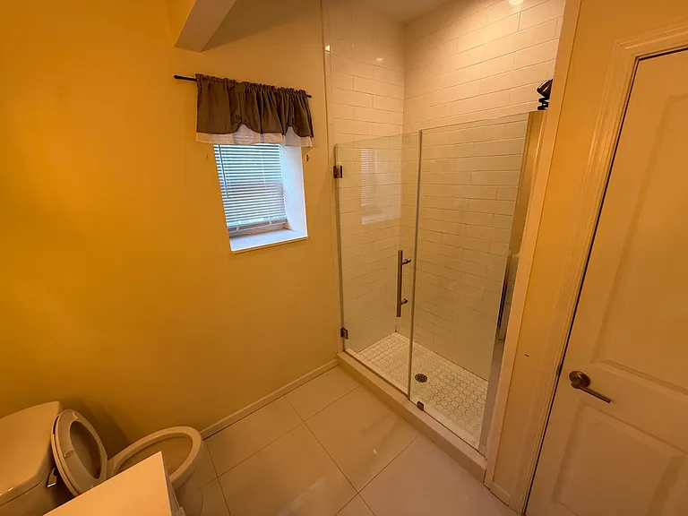 Bathroom features a walk-in glass shower with subway tile surround, tiled flooring, and a window for natural light.