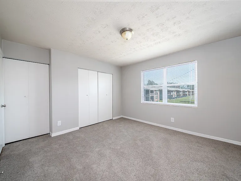 Bright and spacious bedroom with plush carpeting, ample closet space, and a large window offering serene garden views.