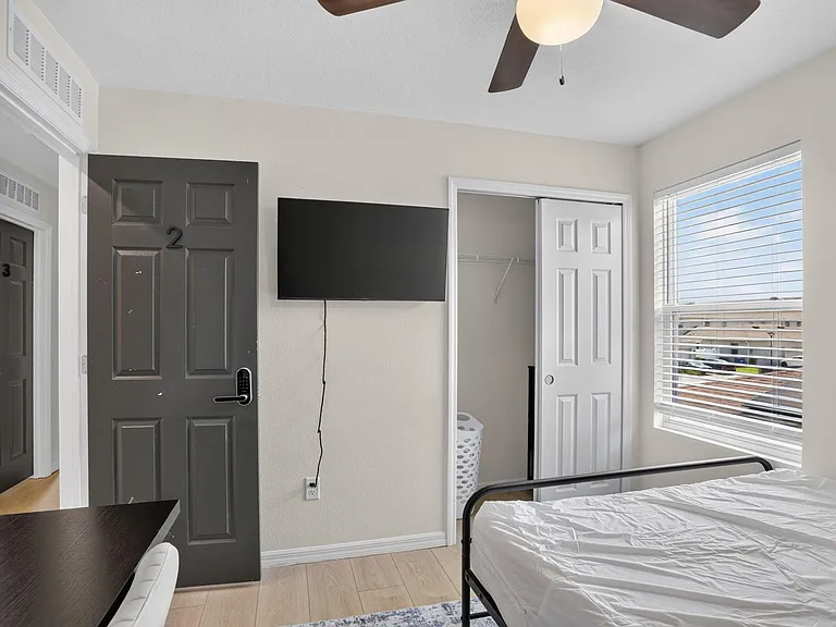 Private bedroom with a window and blinds, ceiling fan, wall-mounted TV, and a closet for convenient storage.