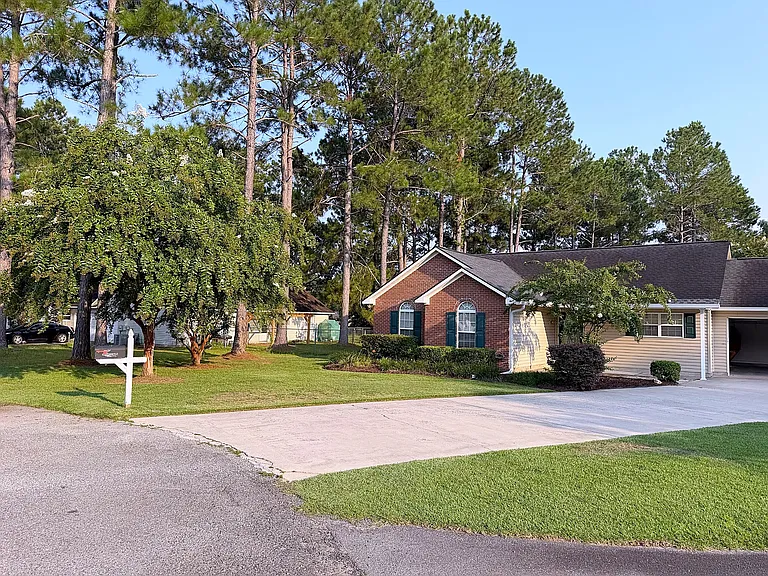 Front exterior with mature trees, attractive landscaping, and a wide driveway