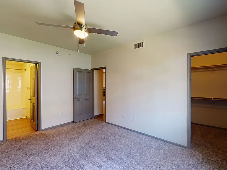 Spacious apartment bedroom with large closet, attached bathroom and plush carpet flooring.
