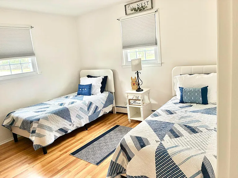 Shared bedroom features two twin beds, hardwood floors, and a nightstand with lamp, plus windows with blinds for privacy.