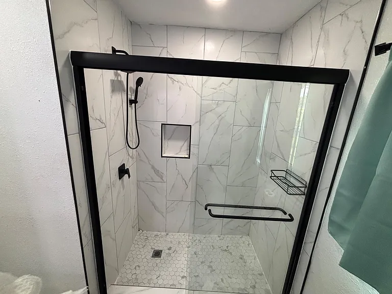 Walk-in shower with marble-look tile surround, glass enclosure, built-in niche, and matte-black fixtures for daily convenienc