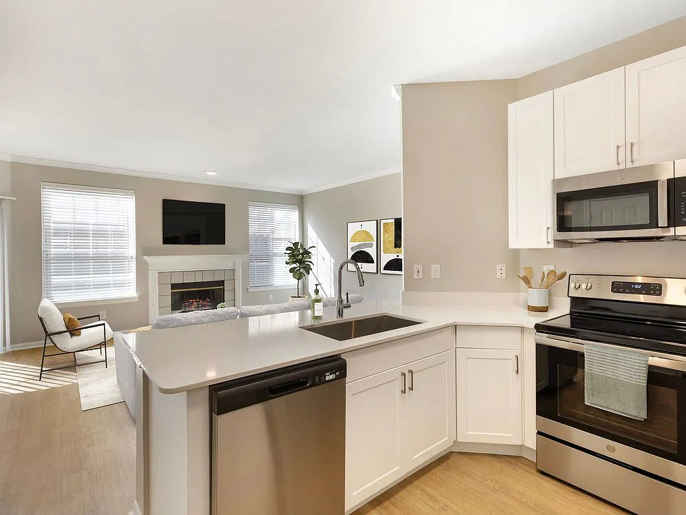 Renovated Package I kitchen with stainless steel appliances, white speckled quartz countertop, white cabinetry, and hard surface flooring - Avalon Addison