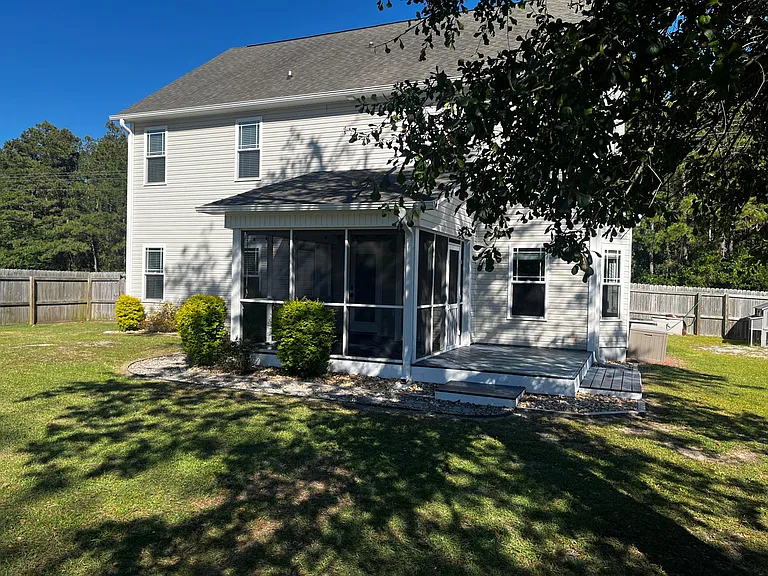 Rear exterior featuring a screened-in porch, deck, and mature landscaping.