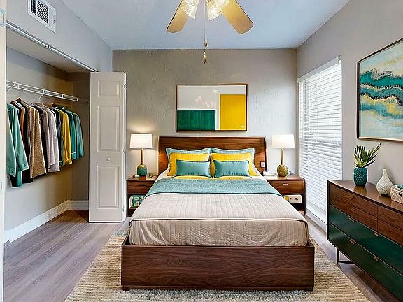 Modern bedroom with sleek wooden furniture, vibrant bedding, and spacious closet, exuding warmth and style.