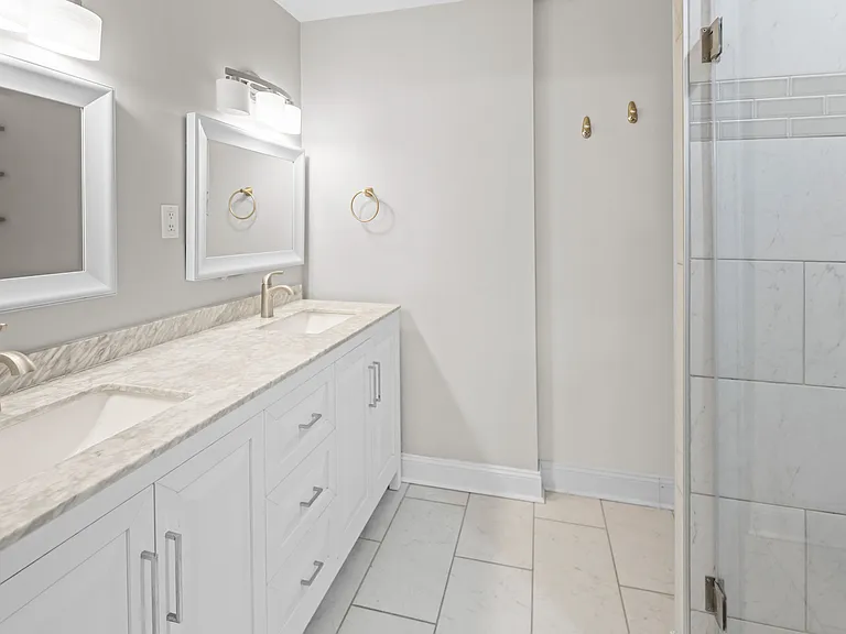 Luxurious master bath with dual vanity sinks, marble countertops, gold accent hardware, and glass-enclosed shower.