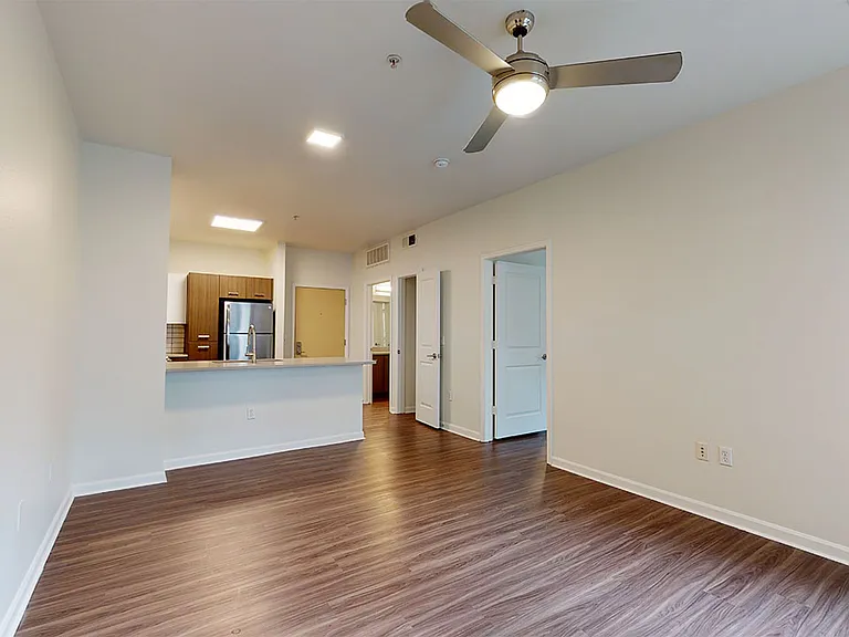 Apartment kitchen with stainless steel appliances, dining and living room with wood-style flooring.