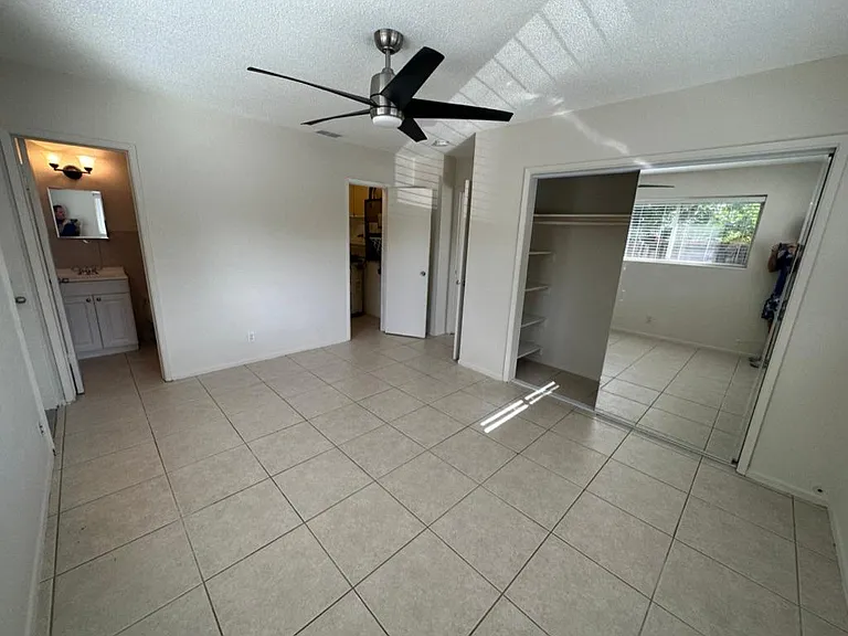 Large Bedroom showing bathroom entry on left, walk in closet ahead behind ceiling fan and wide 2nd closet to right (with mirrored sliding doors - one is open)