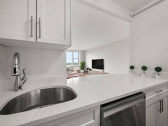 Modern kitchen with sleek stainless-steel appliances, statuario quartz countertops, and six burner gas stove, opening into a bright living area with a large window view at Parkside Place, apartments in Cambridge, MA