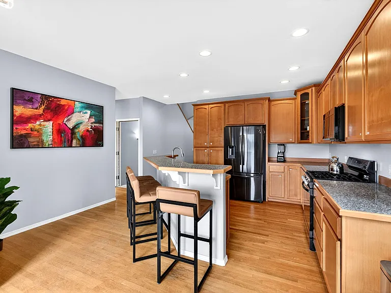 Main floor kitchen features wood cabinetry, stonelook counters, a breakfast bar with seating, and stainless steel appliances.